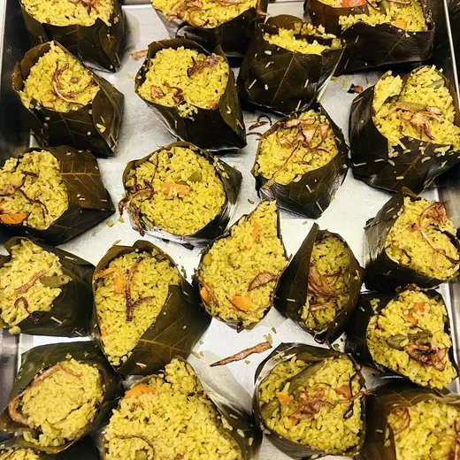 Rice and leaf-parcel preparations from a catering service table.